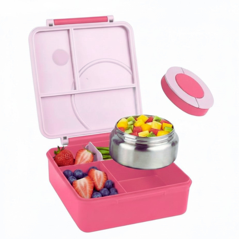 Pink bento box with compartments filled with fruits and a stainless steel bowl on a white background